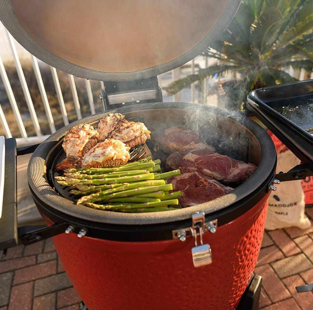Kamado grill with open lid cooking asparagus, steaks, and seafood outdoors in St. Louis, MO