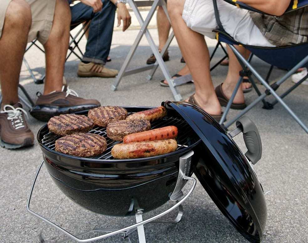 Portable charcoal grill with burgers and sausages cooking at an outdoor gathering in St. Louis, MO